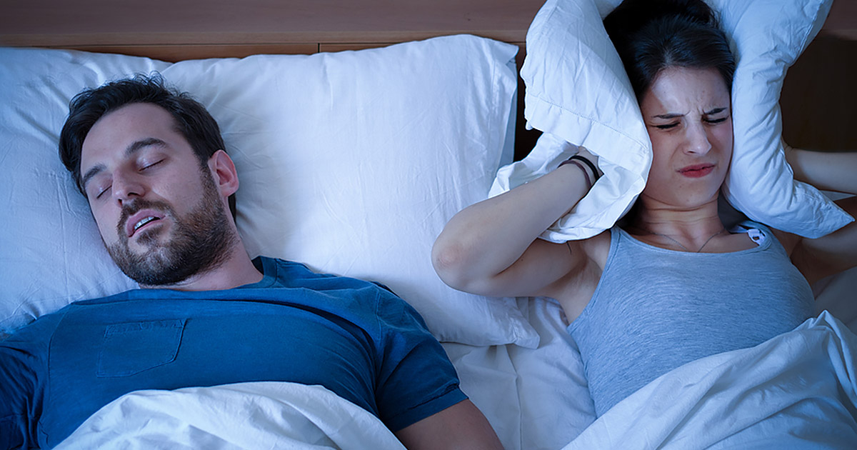 man snoring, wife covering ears while trying to sleep
